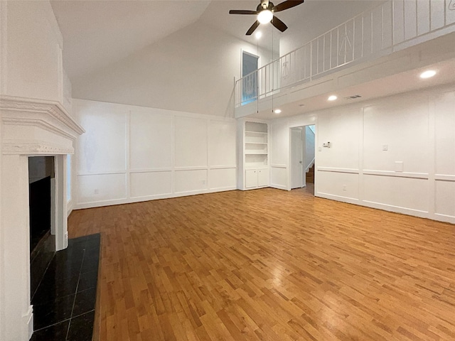 unfurnished living room featuring high vaulted ceiling, built in features, ceiling fan, and wood-type flooring