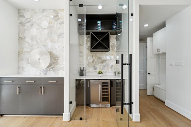 bar featuring white cabinets, beverage cooler, light wood-type flooring, and backsplash