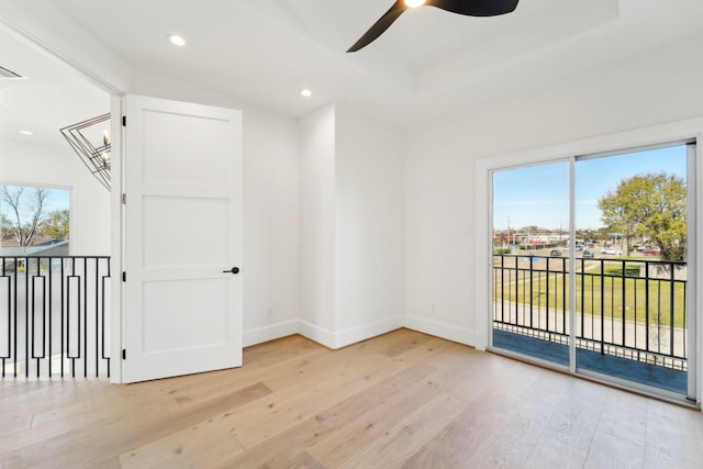 empty room with ceiling fan, light wood-type flooring, and a raised ceiling