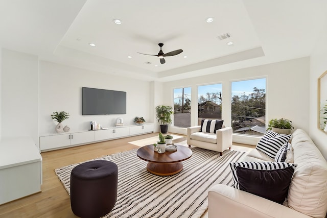 living room featuring light hardwood / wood-style floors, ceiling fan, and a tray ceiling