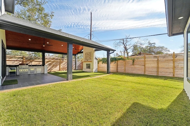 view of yard featuring a patio area, a fireplace, ceiling fan, and exterior kitchen