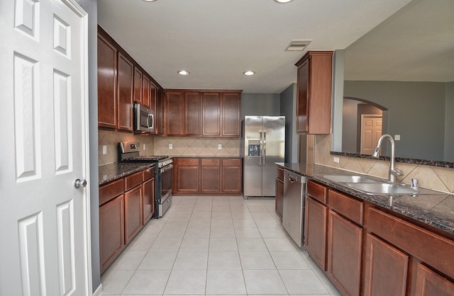 kitchen with stainless steel appliances, dark stone countertops, sink, and light tile patterned floors