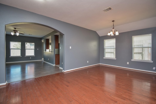 empty room with dark hardwood / wood-style flooring, vaulted ceiling, ceiling fan with notable chandelier, and plenty of natural light