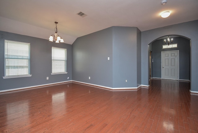 empty room featuring an inviting chandelier, vaulted ceiling, and dark hardwood / wood-style floors