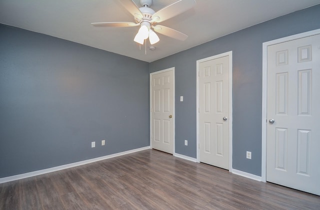 unfurnished bedroom with two closets, ceiling fan, and dark wood-type flooring