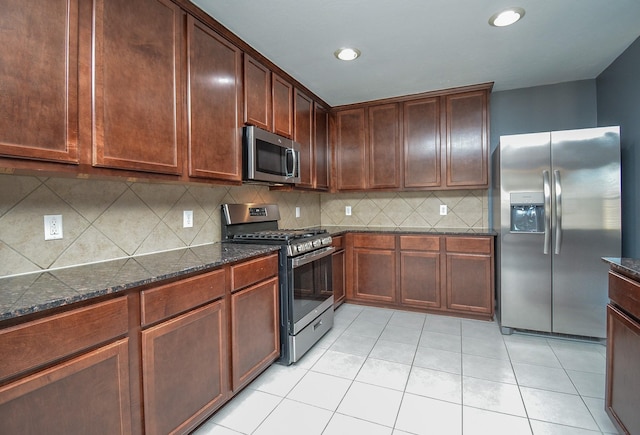 kitchen featuring stainless steel appliances, dark stone countertops, light tile patterned flooring, and tasteful backsplash