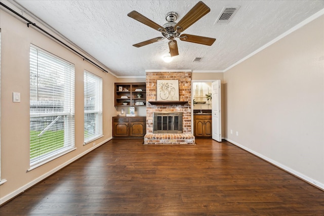 unfurnished living room featuring a fireplace, a textured ceiling, ceiling fan, crown molding, and dark wood-type flooring