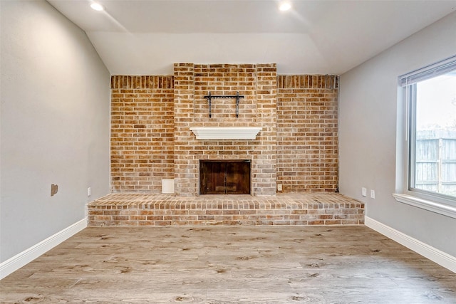 unfurnished living room with lofted ceiling, wood-type flooring, and a brick fireplace