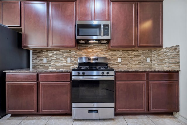 kitchen with stainless steel appliances, light tile patterned floors, dark stone countertops, and backsplash