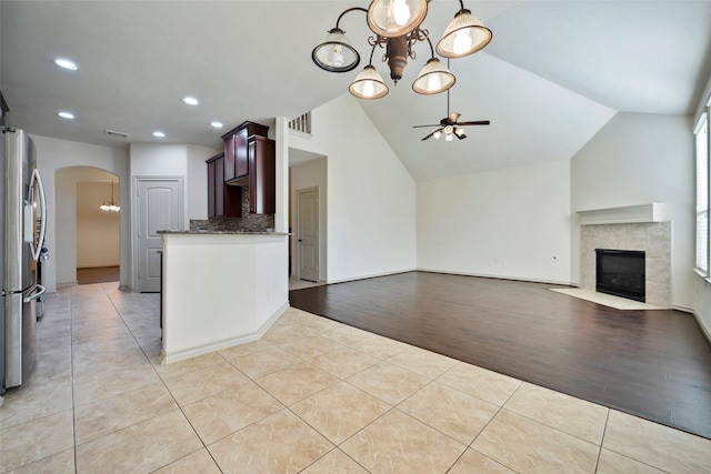 kitchen with vaulted ceiling, stainless steel fridge, ceiling fan with notable chandelier, a high end fireplace, and light tile patterned flooring