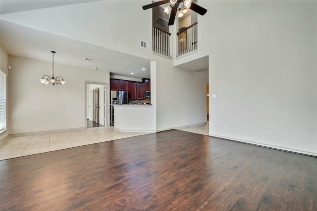 unfurnished living room with ceiling fan with notable chandelier, light hardwood / wood-style flooring, and a high ceiling