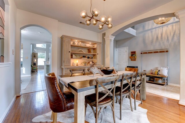 dining room with built in features, light hardwood / wood-style floors, a chandelier, and ornate columns