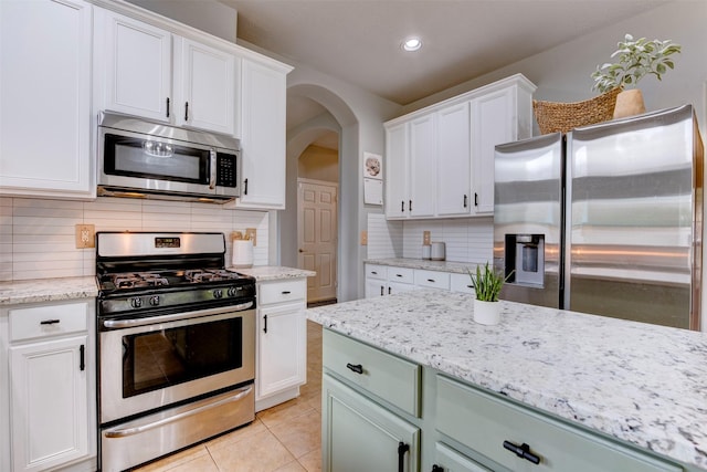 kitchen with light tile patterned floors, white cabinetry, appliances with stainless steel finishes, and arched walkways