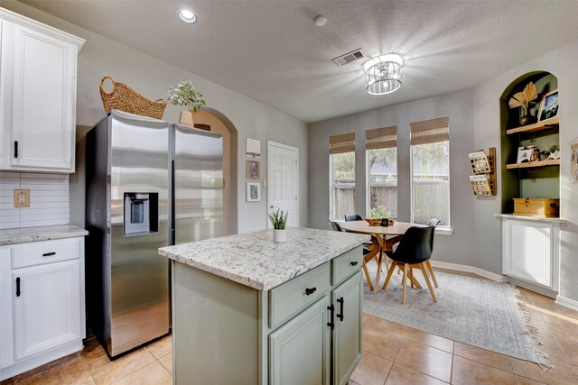 kitchen featuring light tile patterned floors, a kitchen island, stainless steel refrigerator with ice dispenser, white cabinetry, and backsplash