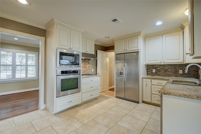 kitchen featuring light tile patterned floors, tasteful backsplash, appliances with stainless steel finishes, ornamental molding, and sink