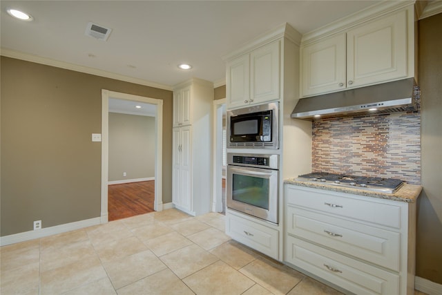 kitchen with appliances with stainless steel finishes, crown molding, light stone countertops, light tile patterned floors, and tasteful backsplash