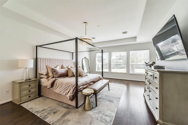 bedroom with an inviting chandelier, a tray ceiling, and dark hardwood / wood-style floors