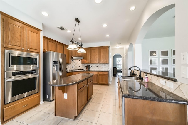 kitchen with hanging light fixtures, a center island with sink, dark stone counters, appliances with stainless steel finishes, and sink