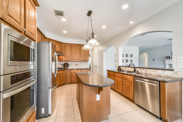 kitchen with stainless steel appliances, a center island, sink, decorative light fixtures, and tasteful backsplash