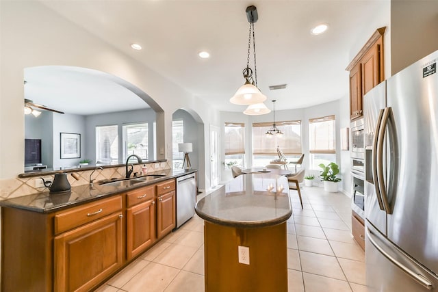 kitchen featuring stainless steel appliances, sink, ceiling fan, a kitchen island, and pendant lighting