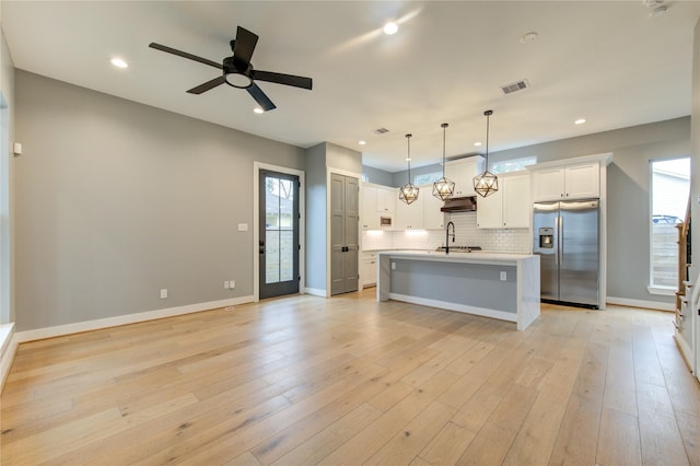 kitchen featuring a kitchen island with sink, light hardwood / wood-style floors, pendant lighting, stainless steel refrigerator with ice dispenser, and sink