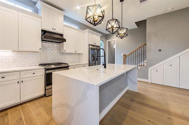 kitchen with a center island with sink, stainless steel appliances, pendant lighting, white cabinetry, and extractor fan