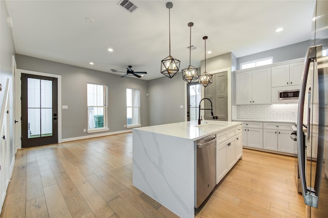 kitchen featuring stainless steel appliances, an island with sink, hanging light fixtures, ceiling fan, and white cabinetry