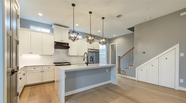 kitchen with light hardwood / wood-style floors, an island with sink, stainless steel fridge, white cabinets, and decorative light fixtures