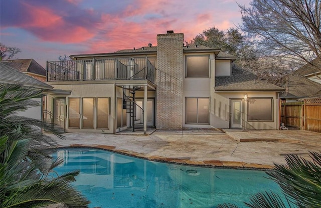 back house at dusk featuring a balcony, a patio area, and a fenced in pool