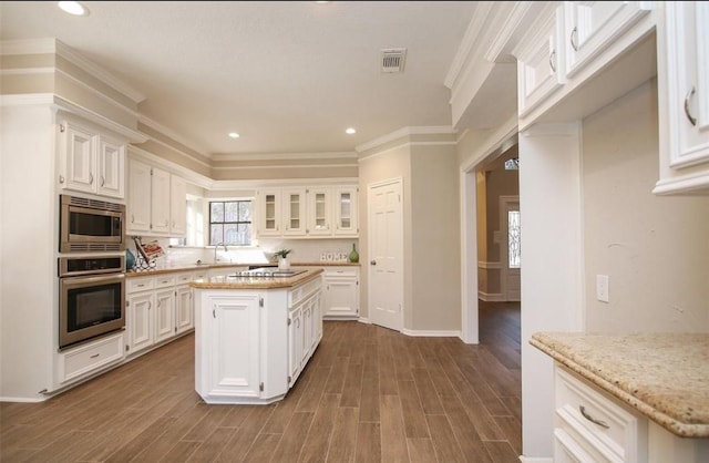 kitchen featuring stainless steel appliances, a kitchen island, white cabinetry, and light stone counters