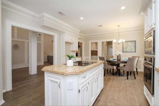 kitchen featuring a center island, pendant lighting, black electric cooktop, stainless steel microwave, and white cabinetry