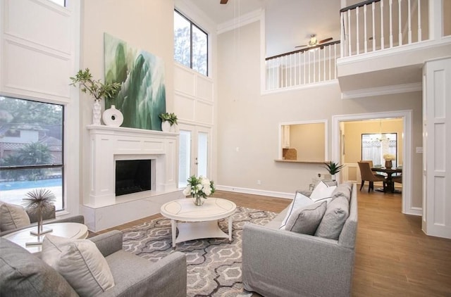 living room featuring a high ceiling, ceiling fan, ornamental molding, and wood-type flooring