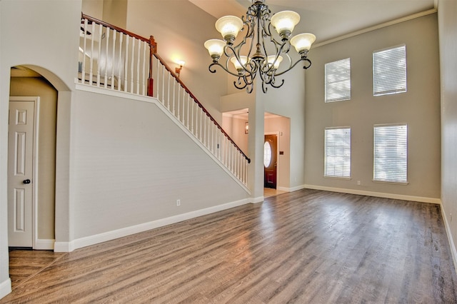 interior space with a towering ceiling, ornamental molding, hardwood / wood-style flooring, and a notable chandelier