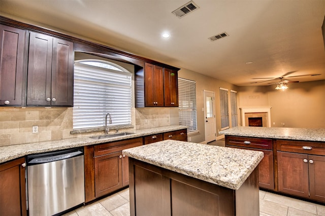 kitchen with light stone counters, stainless steel dishwasher, a tile fireplace, ceiling fan, and sink