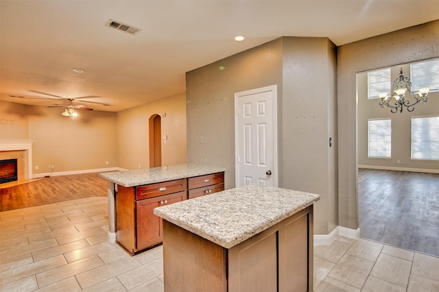 kitchen with light hardwood / wood-style floors, ceiling fan with notable chandelier, light stone countertops, and a kitchen island