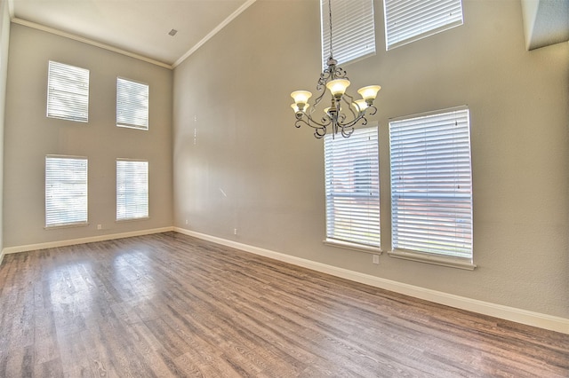 empty room with a towering ceiling, wood-type flooring, an inviting chandelier, and ornamental molding