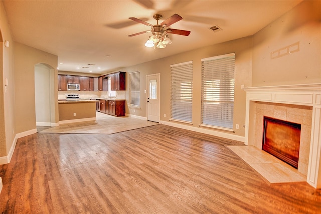 unfurnished living room with ceiling fan, light wood-type flooring, and a tile fireplace