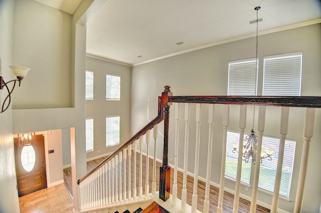 staircase with an inviting chandelier, wood-type flooring, crown molding, and a healthy amount of sunlight