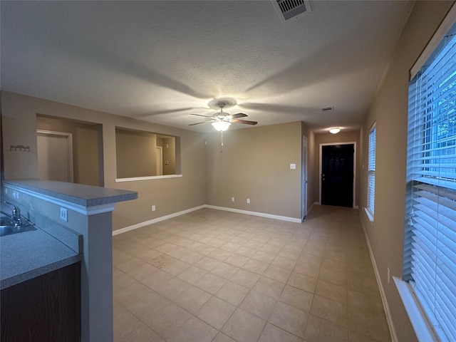 unfurnished living room featuring a textured ceiling, ceiling fan, light tile patterned floors, and sink