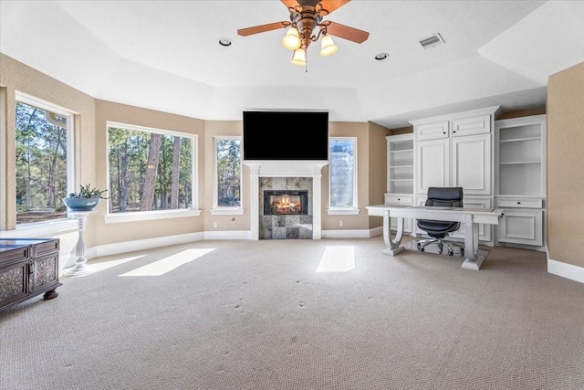 office space with a high end fireplace, ceiling fan, a tray ceiling, and light colored carpet