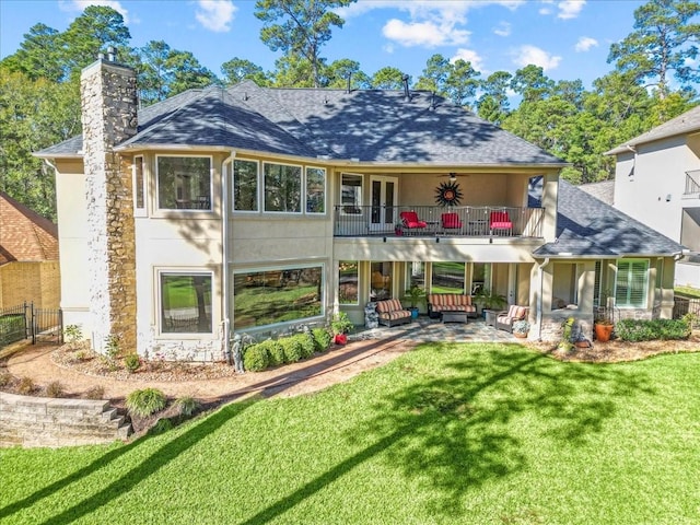 rear view of property with a yard, a balcony, ceiling fan, a patio, and an outdoor living space