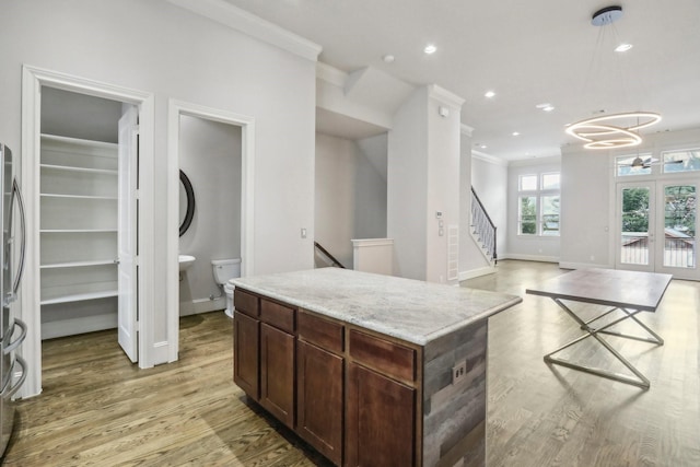 kitchen featuring a center island, light stone counters, french doors, ornamental molding, and light hardwood / wood-style floors