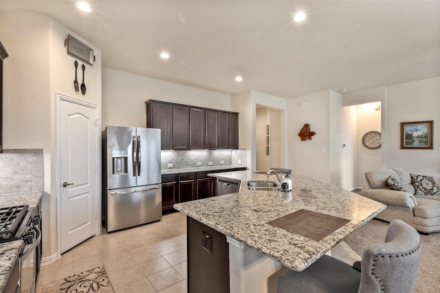 kitchen with sink, tasteful backsplash, dark brown cabinets, an island with sink, and stainless steel appliances