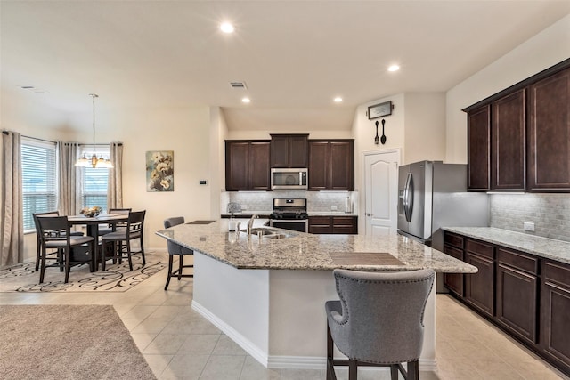 kitchen with decorative light fixtures, sink, light tile patterned floors, stainless steel appliances, and a center island with sink