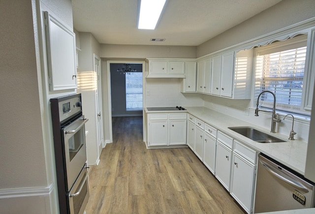 kitchen with white cabinets, light hardwood / wood-style floors, appliances with stainless steel finishes, decorative backsplash, and sink