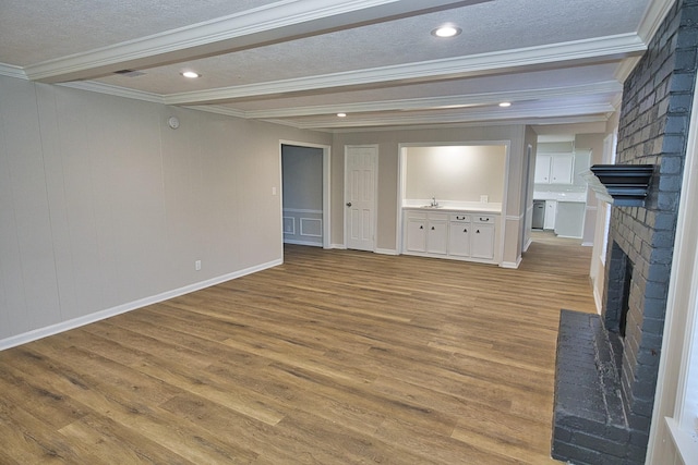 unfurnished living room featuring a textured ceiling, light hardwood / wood-style floors, a brick fireplace, beam ceiling, and crown molding