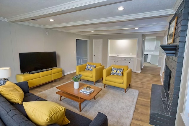 living room with sink, a fireplace, beamed ceiling, light hardwood / wood-style flooring, and crown molding