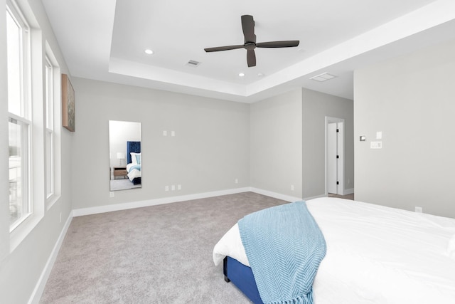 bedroom with ceiling fan, light colored carpet, and a tray ceiling