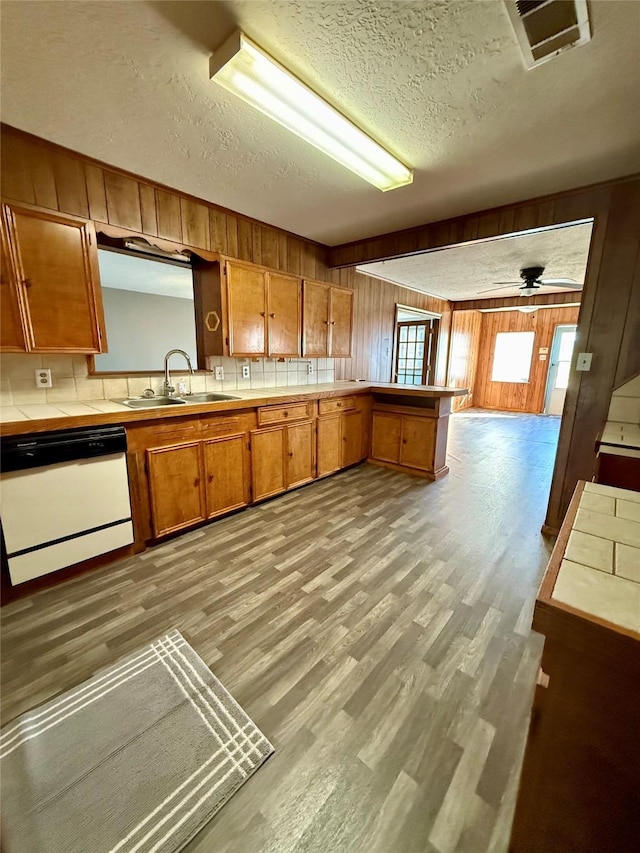 kitchen with sink, dishwasher, ceiling fan, kitchen peninsula, and tile counters