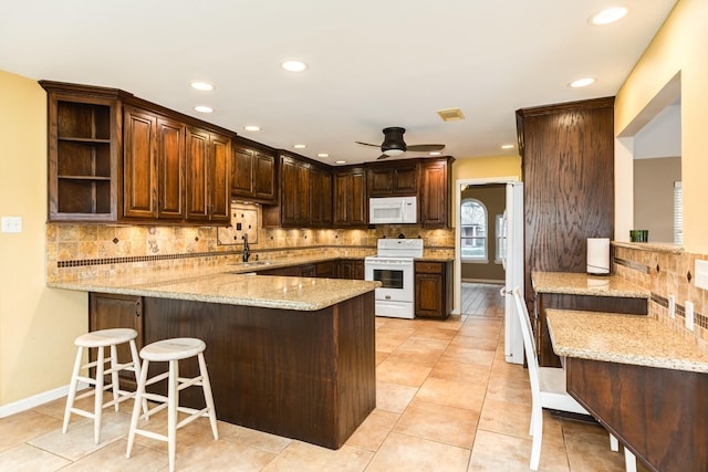 kitchen with a peninsula, a sink, backsplash, a ceiling fan, and white appliances